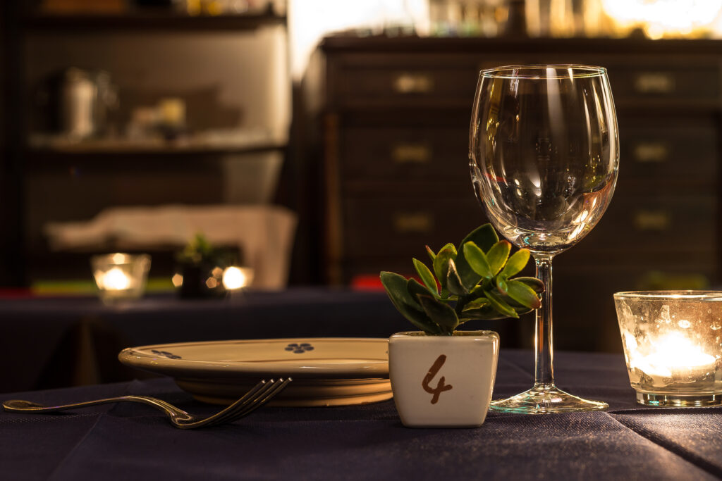 Elegante apparecchiatura con calice da vino, candela e succulenta in vaso su una tovaglia blu navy. Atmosfera calda e accogliente con luci soffuse e sfondo sfocato.