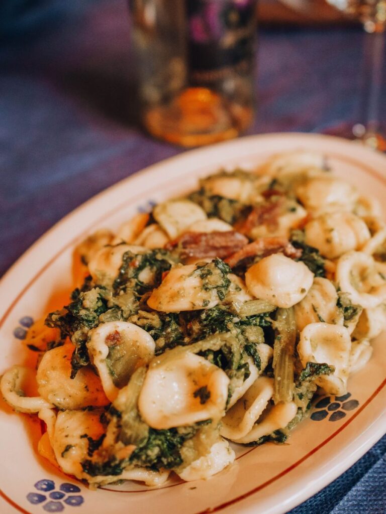 Un piatto di orecchiette alle cime di rapa, piatto tradizionale pugliese, servito su un piatto decorativo. Una bottiglia di vino è sfocata sullo sfondo.
