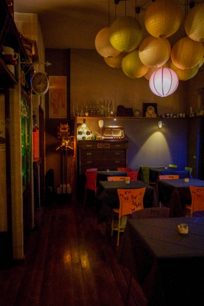 Interno della Vineria Rocca Cellarii a Gioia del Colle con tavoli apparecchiati con tovaglie blu navy e illuminazione bassa e calda resa morbida da punti luce sparsi in tutta la sala