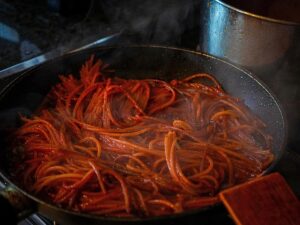 Una pentola fumante di spaghetti conditi con salsa rossa, su un fornello, con un aroma ricco e saporito e un'atmosfera calda e accogliente. Una spatola di legno è appoggiata lì vicino.