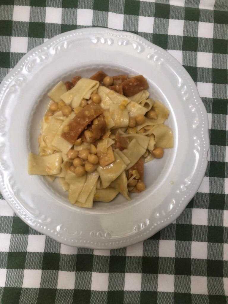 Piatto di ciciri e tria (con pasta fresca ceci e tria fritta croccante), servito in un piatto bianco su tovaglia a quadri verdi e bianchi, in una tipica trattoria leccese.